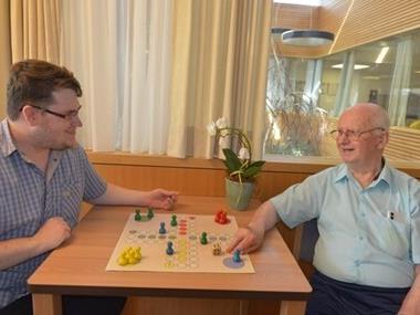 Ein junger Mann spielt mit einem Pensionisten ein Brettspiel
